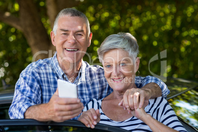 Happy senior couple leaning on car door