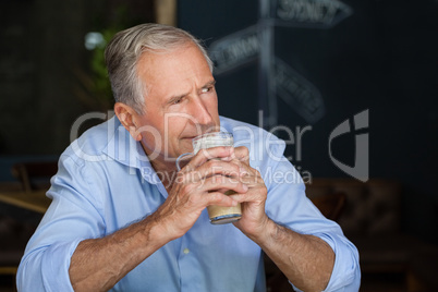 Senior man looking away while holding cold coffee