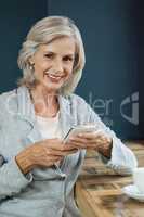 Portrait of smiling senior woman holding mobile phone while sitting at table