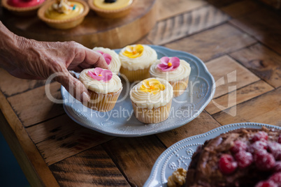 Cropped image of senior woman holding cupcake at table