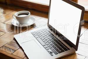 Close up of digital laptop by coffee cup on wooden table
