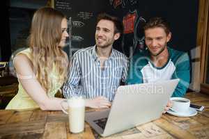 Smiling friends using laptop while sitting at table