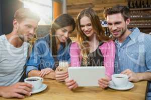 Happy friends using digital tablet while having coffee
