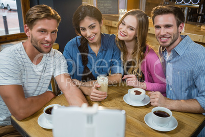 Happy friends taking selfie on mobile phone while having coffee