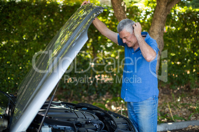 Senior man checking engine of breakdown car