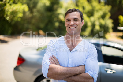 Man with arms crossed standing by car