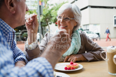 Senior woman feeding sweet food to man in cafÃ?Â©