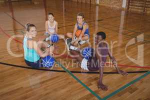 Smiling high school team relaxing in the basketball court