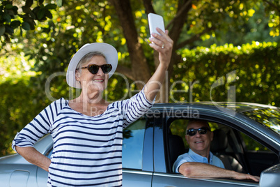 Senior woman taking selfie with man sitting in car