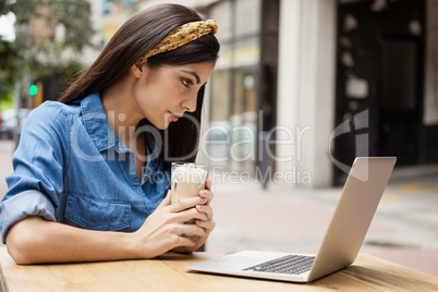 Woman using laptop computer while holding cold coffee