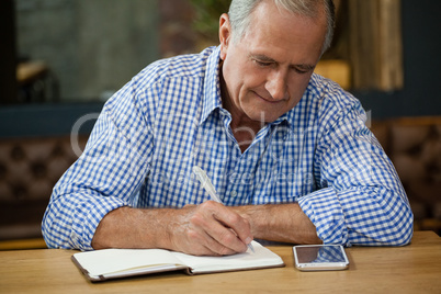 Senior man writing on diary at table