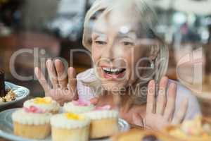 Close up of happy woman looking at cupcakes seen through glass window