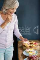 Smiling woman holding cupcakes while standing at table