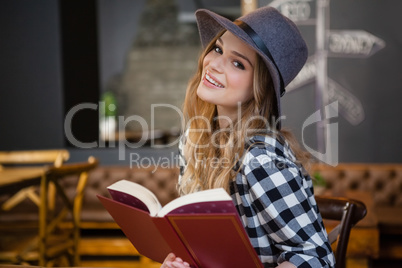 Portrait of cheerful woman holding book while sitting on chair