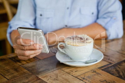 Cropped image of person holding smart phone while sitting by coffee cup