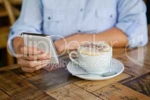 Cropped image of person holding smart phone while sitting by coffee cup