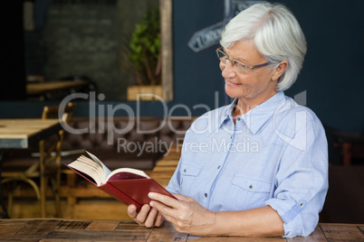 Smiling senior woman reading book while sitting by table