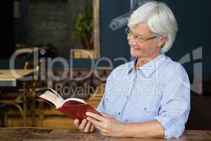 Smiling senior woman reading book while sitting by table