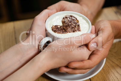 Cropped imageof couple holding coffee cup at wooden table