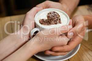 Cropped imageof couple holding coffee cup at wooden table