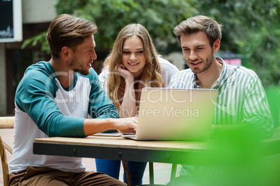 Happy friends using laptop while sitting on chair