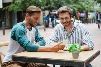 Friends using smart phone while sitting at sidewalk cafe