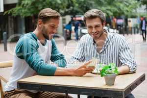 Friends using smart phone while sitting at sidewalk cafe