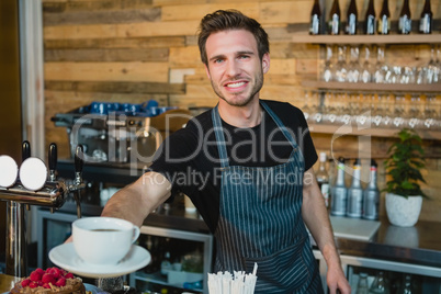 Portrait of smiling waiter offering cup of coffee at counter