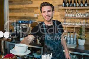 Portrait of smiling waiter offering cup of coffee at counter