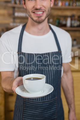 Smiling waiter offering cup of coffee