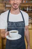 Smiling waiter offering cup of coffee