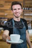 Smiling waiter offering cup of coffee at counter