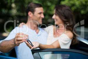 Man giving key to woman by car