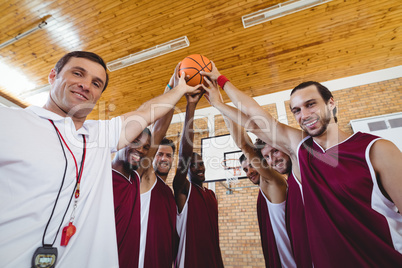 Players and coach holding basketball together in the court