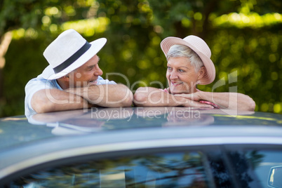Senior couple looking at each other while leaning on car roof