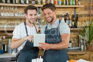 Smiling waiters using digital tablet at counter