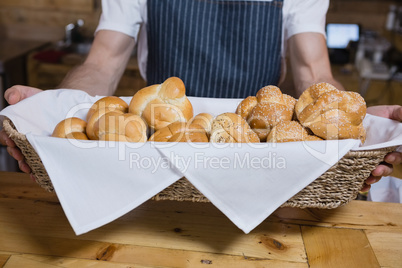 Mid section of waiter holding basket of baked pastries at counter