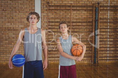 Confident high school boys holding basketball in the court