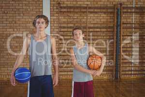 Confident high school boys holding basketball in the court