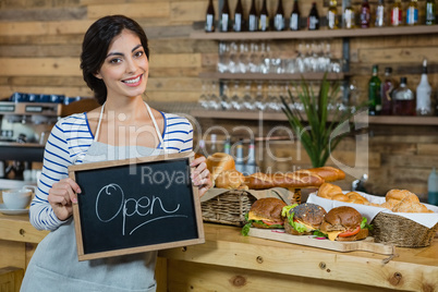 Portrait of waitress holding open signboard at counter