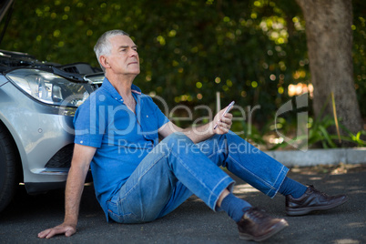 senior man sitting by car on road after breakdown