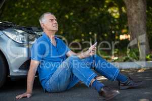 senior man sitting by car on road after breakdown