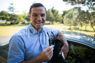 Young man holding mobile phone and sunglasses by car
