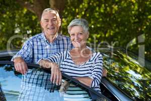 Smiling senior couple leaning on car door