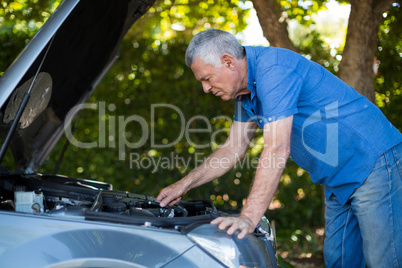 Senior man checking engine of breakdown car