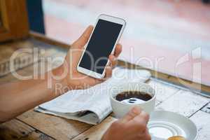 Cropped image of woman holding mobile phone while drinking coffee