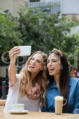 Cheerful friends photographing while sitting at sidewalk