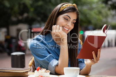Woman reading book while sitting on chair at cafe shop