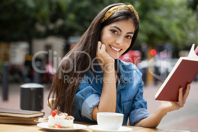 Portrait of woman reading book while sitting on chair at cafe