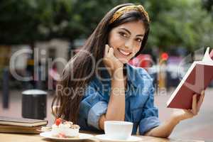 Portrait of woman reading book while sitting on chair at cafe